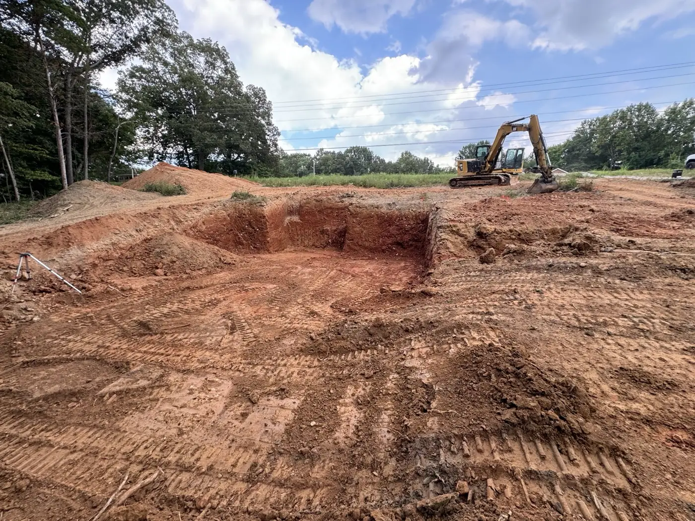 Excavator beside a foundation dig in red clay on a Middle Tennessee job site