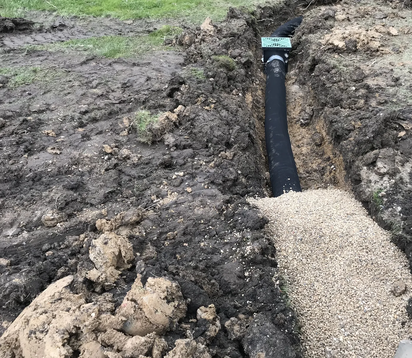 Perforated drain pipe in a trench with washed gravel backfill going in