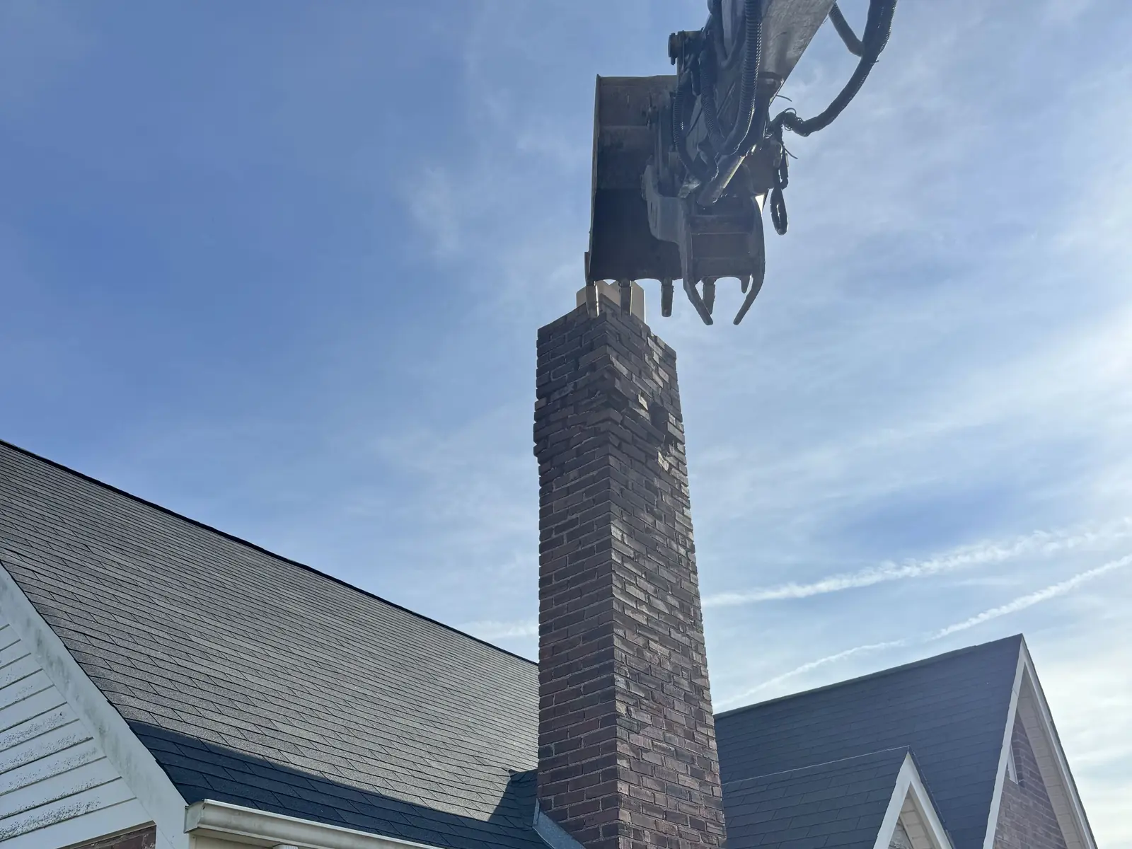 Excavator thumb pulling the brick chimney off a house during demolition