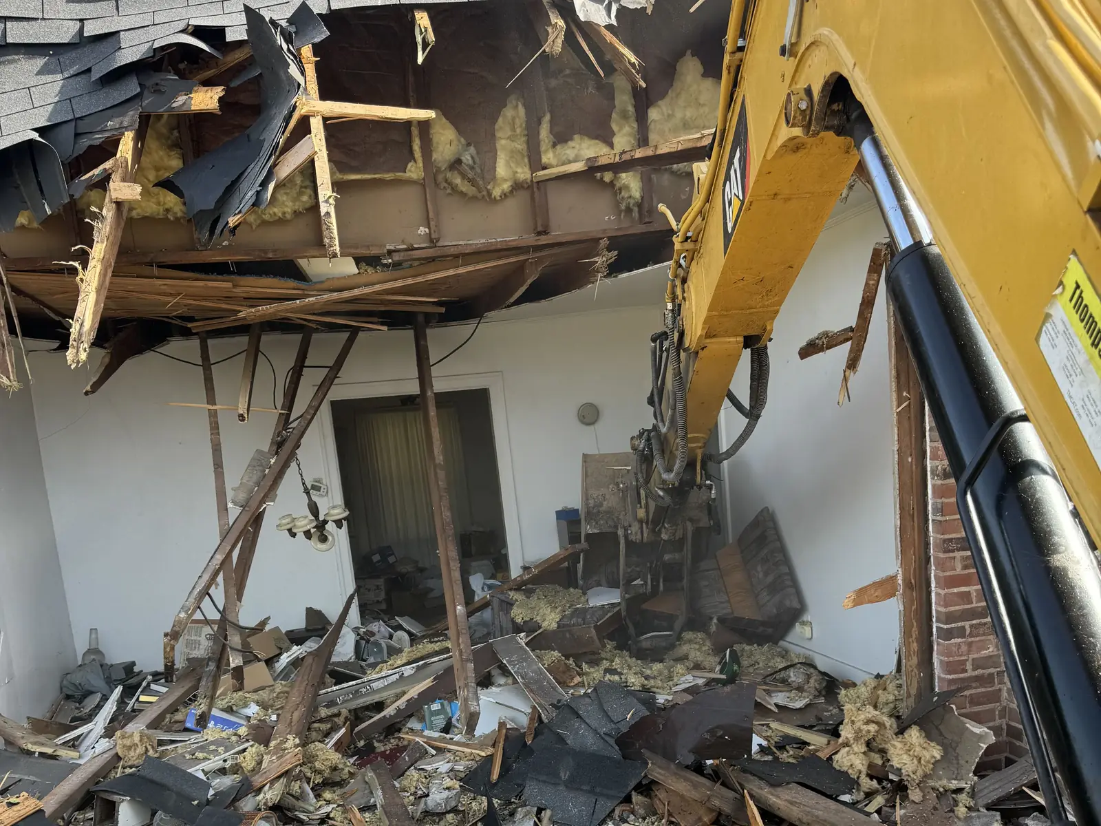 Excavator boom through the torn-open roof, insulation and broken rafters hanging