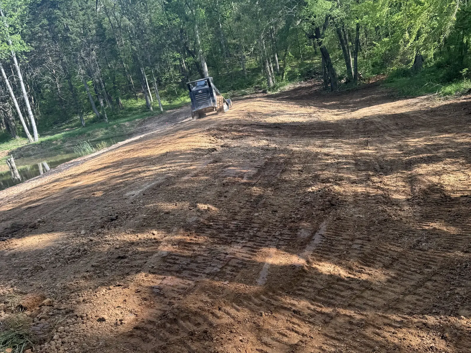 Finished dam top graded smooth, the compact track loader at the far end and straw along the water side