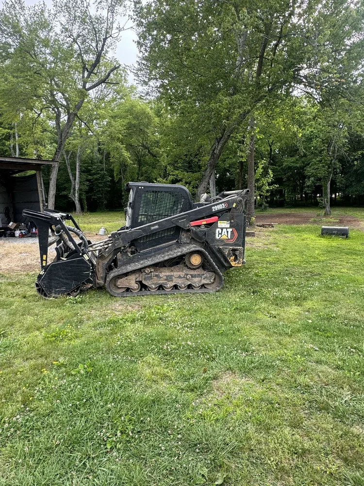 Tracked skid steer with the forestry mulcher head parked on the grass